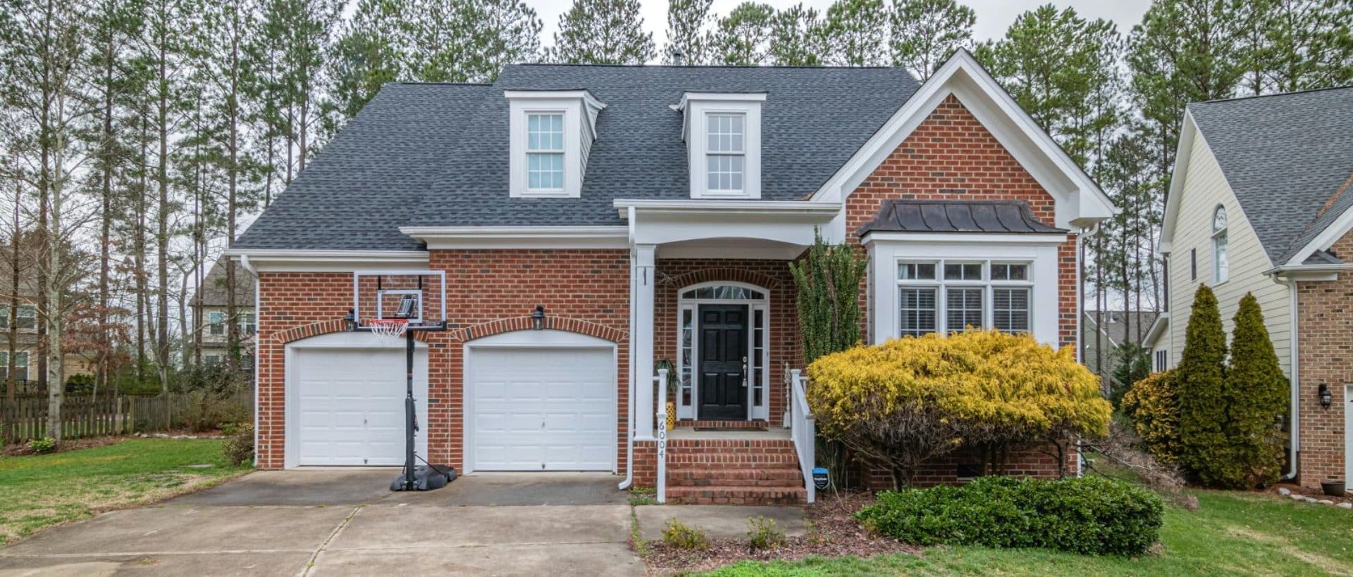 A house with a basketball hoop and trees in the background.
